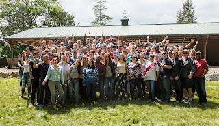 Large group of people posing on a lawn in front of a pavilion.